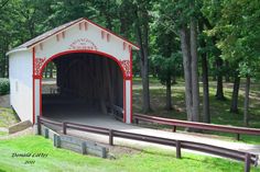 a red and white covered bridge in the middle of a park with trees around it