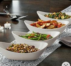 four white bowls filled with food on top of a table next to candles and utensils