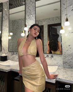 a woman standing in front of a bathroom mirror wearing a gold skirt and matching top