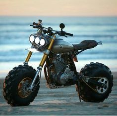 the motorcycle is parked on the beach by the water's edge with its lights on