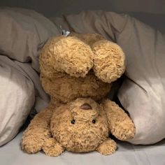 two brown teddy bears sitting on top of each other in bed with white sheets and pillows