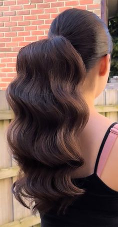 the back of a woman's head with long, wavy hair in front of a brick wall