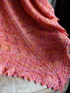 an orange and pink shawl on top of a white chair next to a window