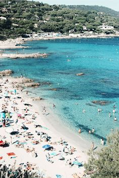 many people are laying on the beach and swimming in the blue water, some with umbrellas