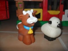 two toy farm animals sitting next to each other on the floor in front of a play house