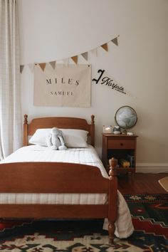 a bed sitting in a bedroom next to a window with white curtains and bunting