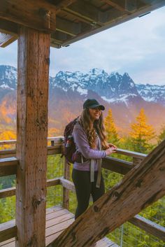 a woman is standing on a wooden deck with mountains in the background