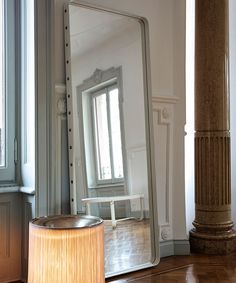 a large mirror sitting on top of a wooden floor next to a lamp and window