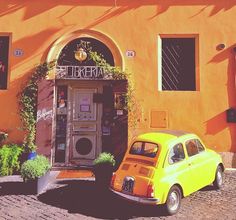 an old yellow car parked in front of a building with plants growing out of it