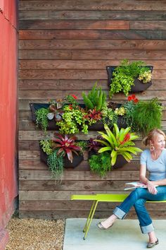 a woman sitting on a bench in front of a wooden wall with plants growing on it