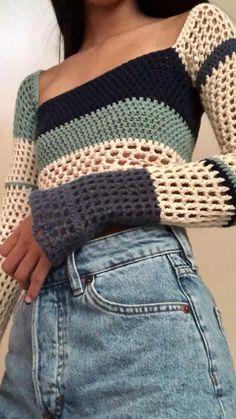 a woman is wearing a crocheted sweater and denim skirt with her hand on her hip