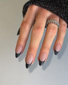 These nails stand out with a sleek black glitter French tip on a nude base, perfect for a bold winter look. The almond shape gives it elegance, while the dark glitter adds a touch of glamour. This design is ideal for anyone looking to blend simplicity with a bit of edge. Black Glitzy Nails, Little Black Heart Nails, Black Sparkly French Tips, Dark Festive Nails, Black French Glitter Nails, Glitter Base French Tip, New Years Black Nails, Silver French Tip Nails Almond, Black Glitter Nails French Tips