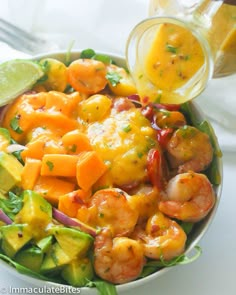 shrimp, avocado, and mango salad in a white bowl with dressing being drizzled on top