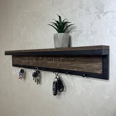 a wooden shelf with key hooks and some keys hanging on the wall next to a potted plant