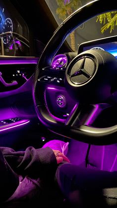 the interior of a car is lit up with purple lights and features steering wheel controls