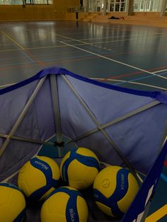 several yellow and blue soccer balls in a basket on the floor inside an indoor gym