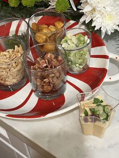 several bowls filled with different types of food on a red and white plate next to flowers