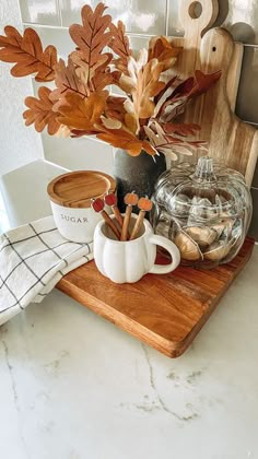 a wooden cutting board topped with a cup filled with leaves