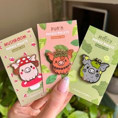 three pin badges with animals on them sitting in front of a green potted plant