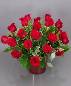 a vase filled with lots of red roses on top of a gray table next to a wall