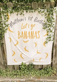 a birthday banner with bananas hanging on a fence in front of some plants and vines