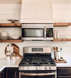 a stove top oven sitting inside of a kitchen next to wooden shelves with dishes on them