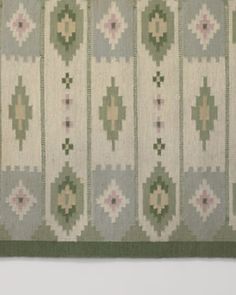 an old quilt hanging on the wall in front of a white wall with green and pink designs