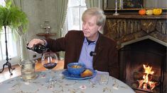 an older man pouring wine into a blue bowl at a table with food on it