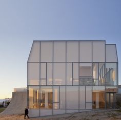 a man walking past a large glass building on top of a sandy beach next to the ocean