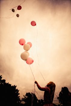 a woman holding onto some balloons in the air