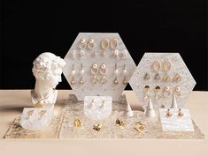 an assortment of jewelry on display in front of a white sculpture with gold earring hooks