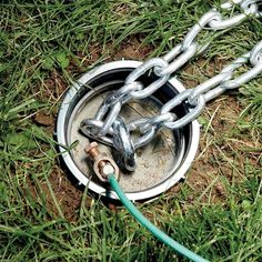 a metal chain connected to a water well in the grass with a hose attached to it