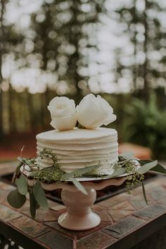 a white cake sitting on top of a table covered in greenery and topped with flowers