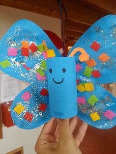 a hand holding up a blue butterfly made out of construction paper and colored stickers