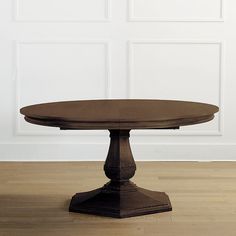 a round wooden table sitting on top of a hard wood floor next to a white wall