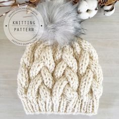 a knitted hat with a fur pom on top of it next to cotton flowers