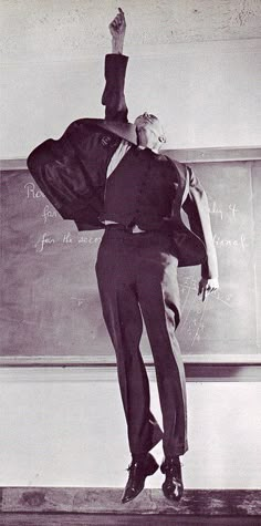 an old photo of a man standing in front of a chalkboard with his arms outstretched