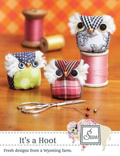 three small owls sitting on top of a table next to spools of thread