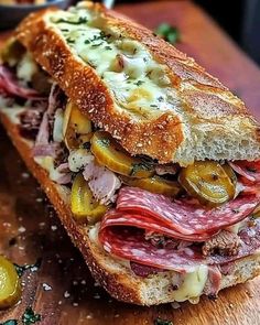 a sandwich with meat, cheese and vegetables on it sitting on a wooden cutting board