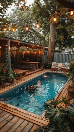 an outdoor swimming pool surrounded by wooden decking and lights hanging from the tree branches