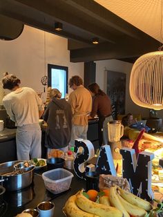 a group of people standing in a kitchen next to a counter filled with bananas and other food