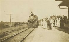 an old black and white photo of people standing next to a train on the tracks