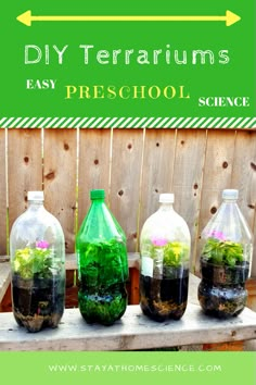 three glass bottles filled with plants and dirt on top of a wooden table next to a fence