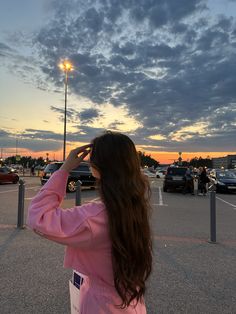 a woman standing in the middle of a parking lot looking up at a sky filled with clouds