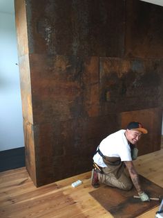 a man kneeling on the floor in front of a large piece of wood that is being worked on