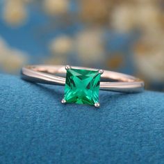 a ring with a square cut green stone in the center on a blue cloth background