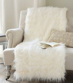 a white chair with a book on top of it next to a pillow and some pillows