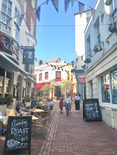 people are walking down the sidewalk in front of shops and restaurants on a sunny day