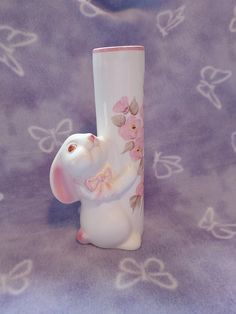 a white vase with pink flowers on it and a bunny figurine next to it