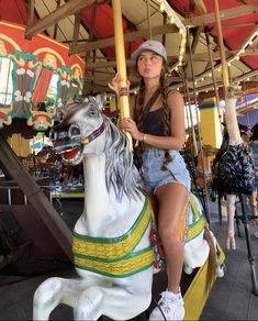 a woman sitting on top of a merry go round horse at an amusement park,